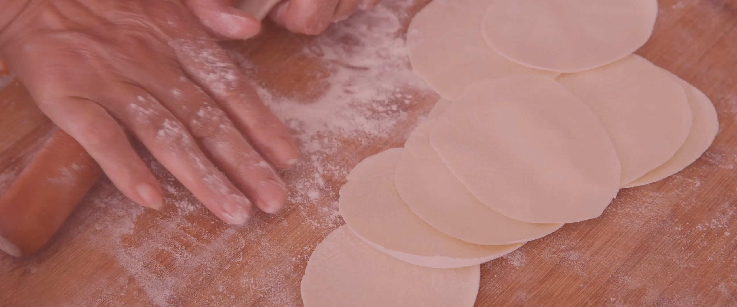 Manos amasando y preparando discos de pasta para empanadas sobre mesa enharinada de madera