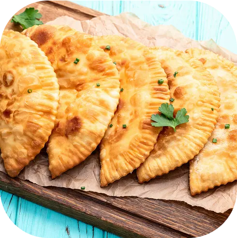 Empanadas fritas doradas de La Chilenita servidas sobre bandeja de madera con hojas de perejil.