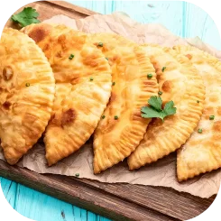 Empanadas fritas doradas de La Chilenita servidas sobre bandeja de madera con hojas de perejil.